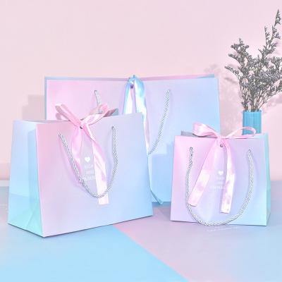 China Recyclable Paper Bag Shopping Bags Custom Logo Printed Gradient Color Pink Blue Reusable Glitter Gift Bag With Bow Ribbon Wedding Party for sale