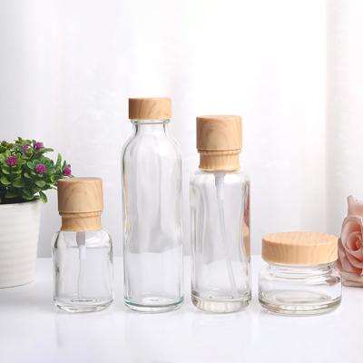 China Eco-friendly Unique Clear Glass Jar 100g 50ml 150ml Cream Cosmetic Glass Bottles Lotion Bottle Set With Wood Grain Lid for sale