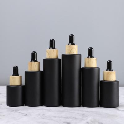 China Cosmetic Refillable Frosted Cylinder Matte Black Glass Dropper Bottle Cosmetic for Essential Oil Pipette Container with Wood Grain Lid for sale