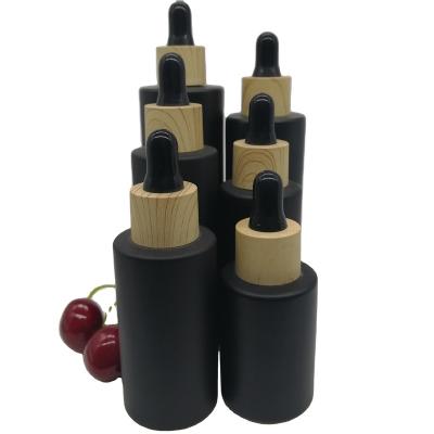 China Cosmetic Matte Black Coating Dropper Bottle Essential Oil Glass Bottle With Wood Grain Dropper Cap for sale