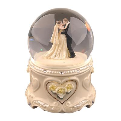 China Crystal Ball Merge With Music Box Gift For Girlfriend Or Wife Wedding Souvenirs Ceramic Wedding Theme Water Snow Globe Custom Music Box for sale