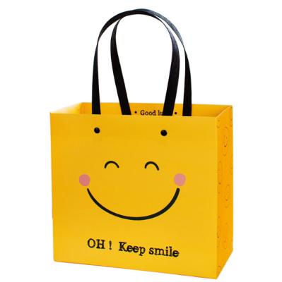 China Recyclable Yellow Smile Paper Bag T-shirt Clothing Shopping Paper Packaging Bag With Handle for sale